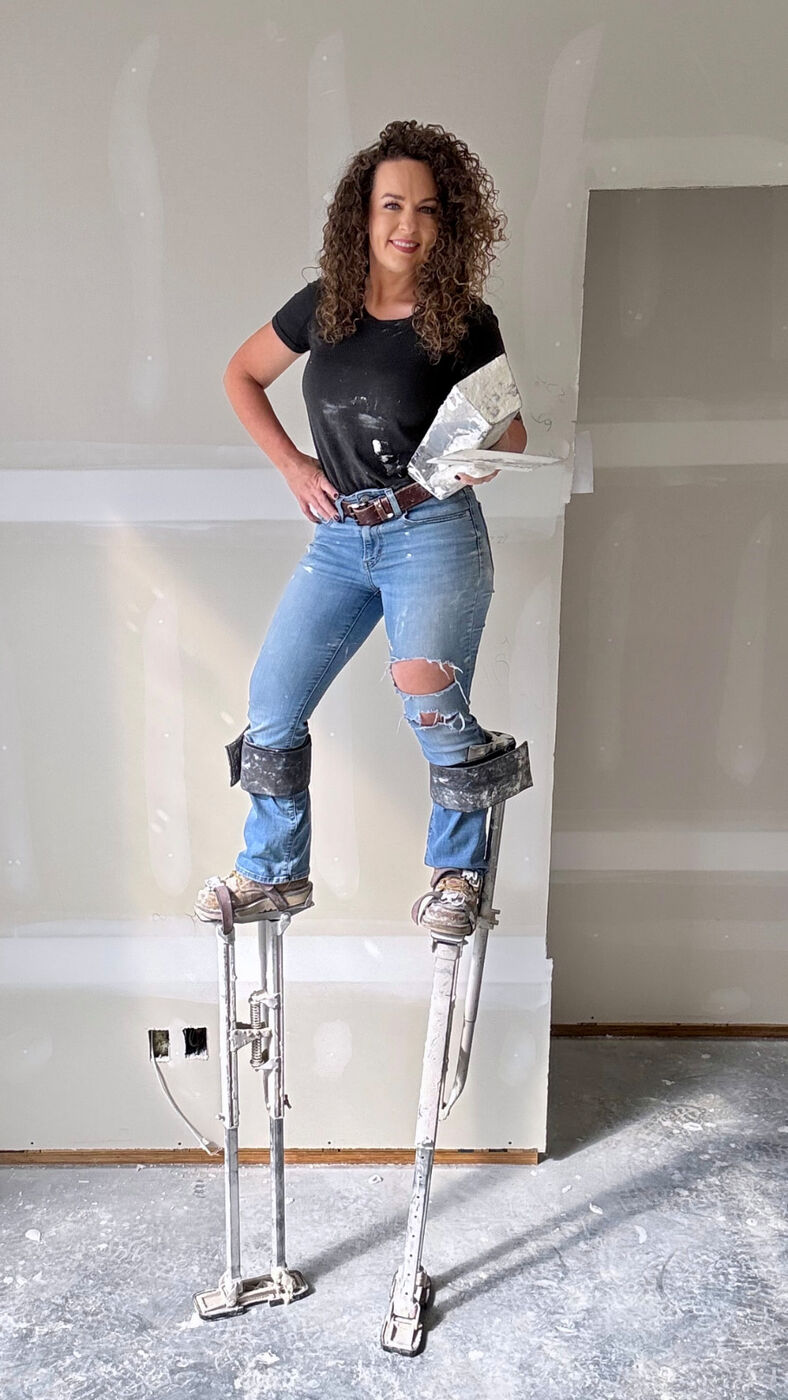 Lydia on drywall stilts holding a mud pan and knife